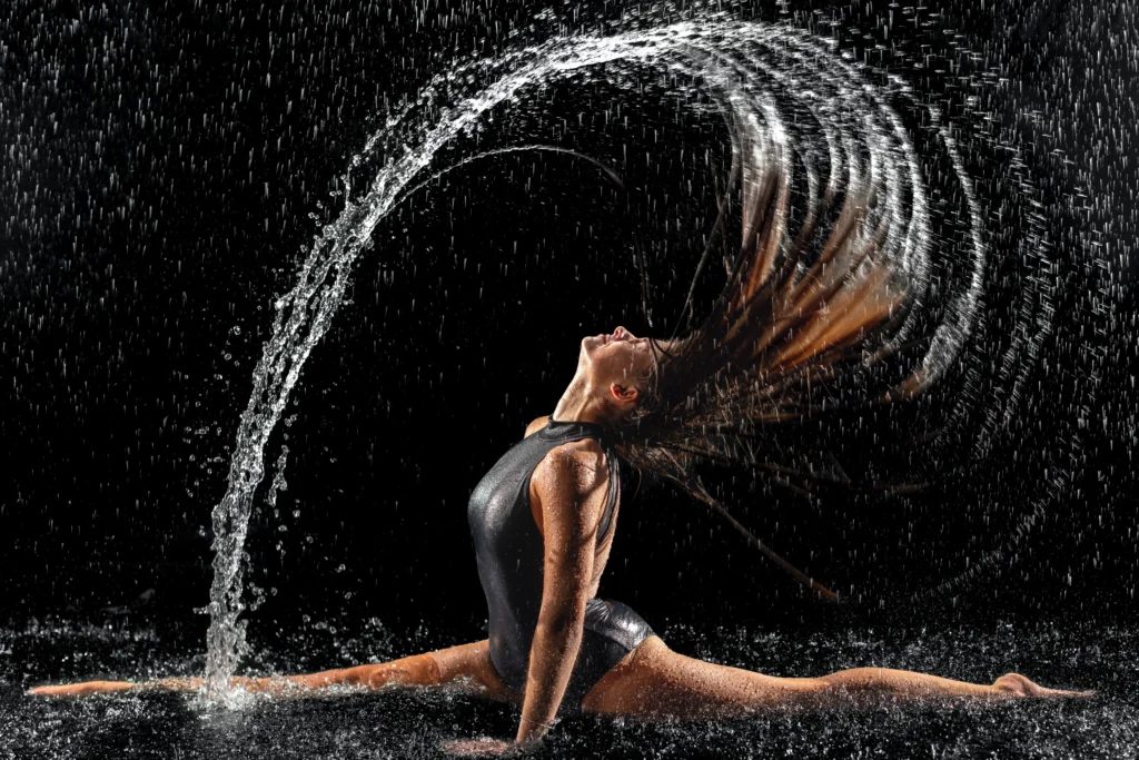 Auf diesem Bild kann man eine Tänzerin sehen die ihren Kopf mit Wasser reinigt, indem Sie mit Schwung die Haare von vorne nach hinten wirft.